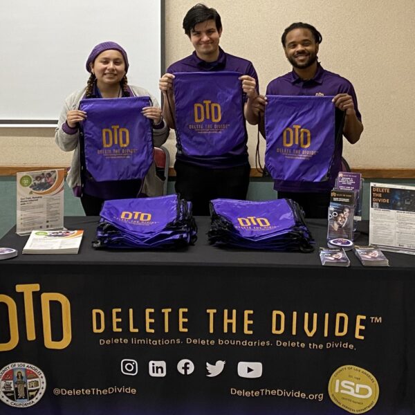 three DTD interns holding up drawstring bags behind a DTD table with flyers and more bags