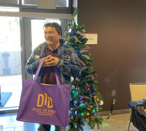 Man with jacket holding DTD bag in front of christmas tree