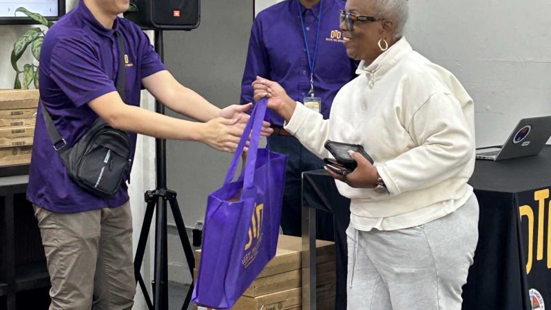 DTD staff handing bag to a participant with two other staff in the back