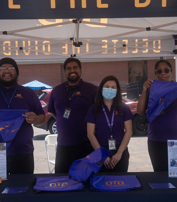 four DTD staff members standing behind a table with bags, lanyards, and flyers