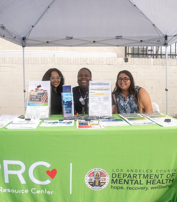 three women sitting behind a Peer Resource Center booth by L.A. County D.M.H.