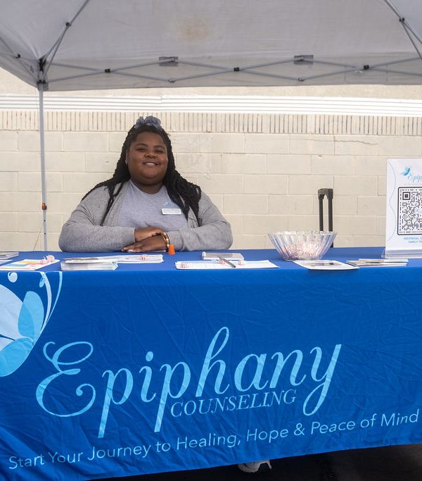 a woman smiling and sitting behind the Epiphany Counseling booth