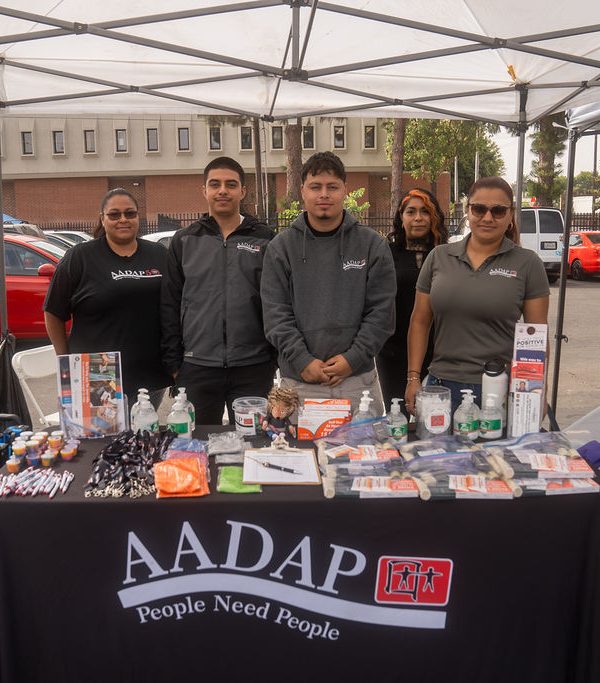 five people standing behind a AADAP (Asian American Drug Abuse Program) booth