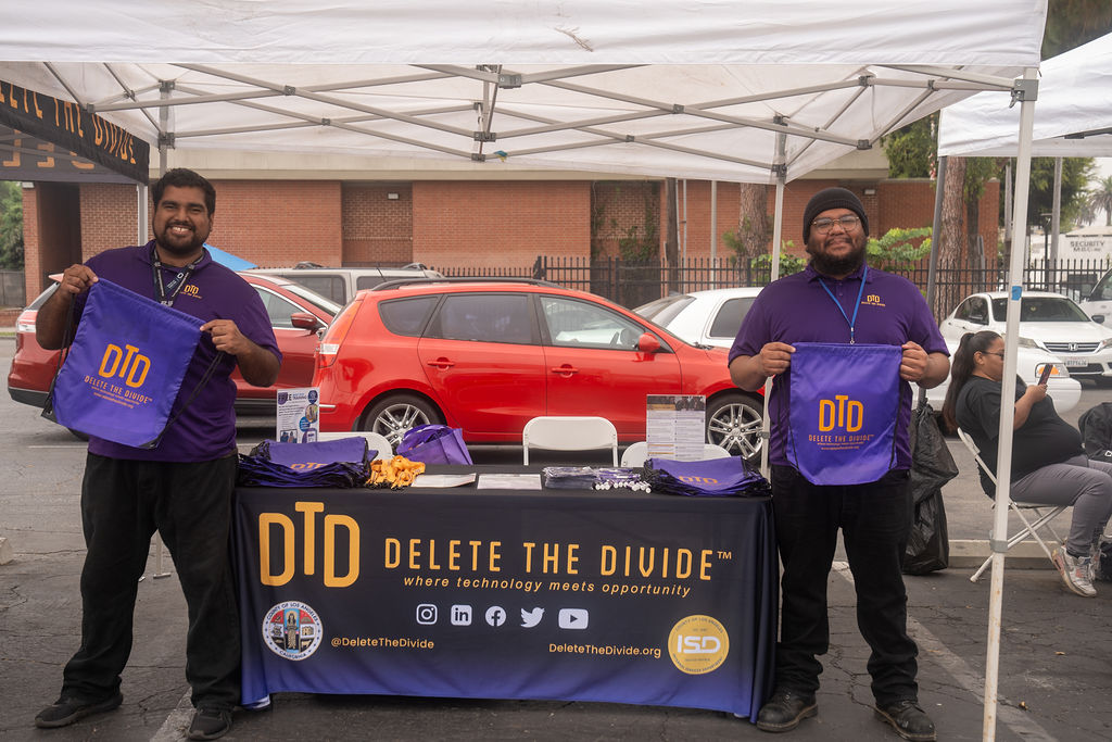 two DTD interns holding up DTD bags standing beside a table with bags, lanyards, and flyers