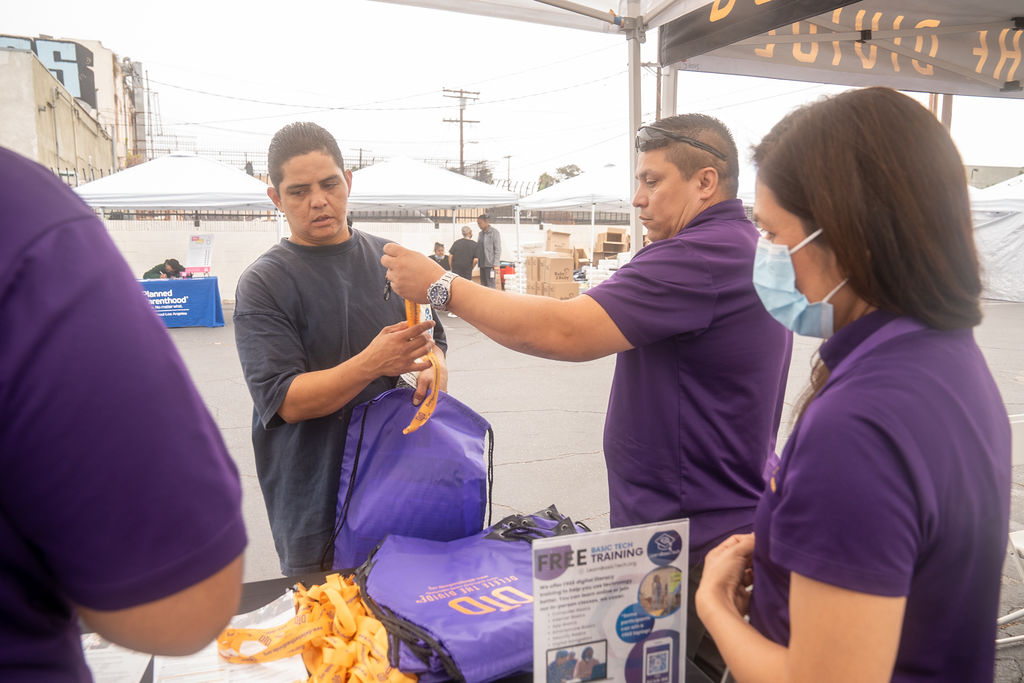 three DTD staff members passing out DTD bags and lanyards to a person