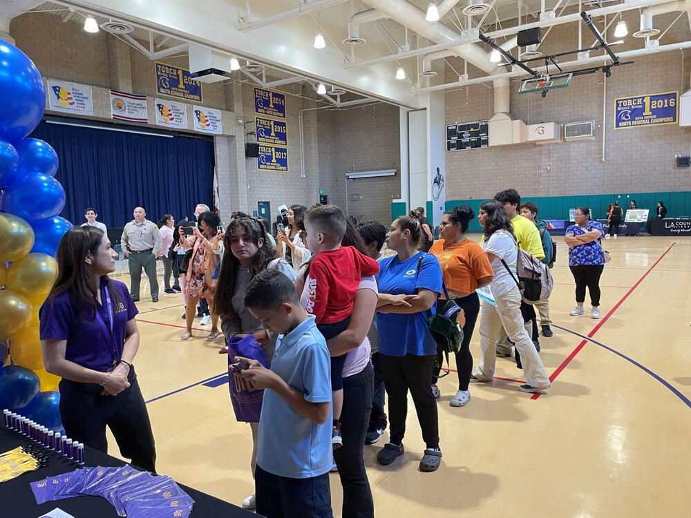 students and parents lining up to receive things at the DTD table booth in a middle school gym
